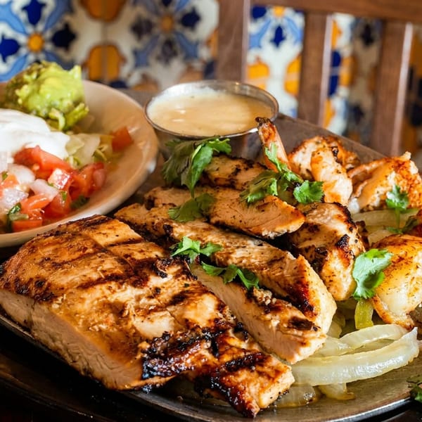 Grilled chicken, steak, and shrimp platter with sautéed onions, cilantro, creamy sauce, guacamole, and pico de gallo.