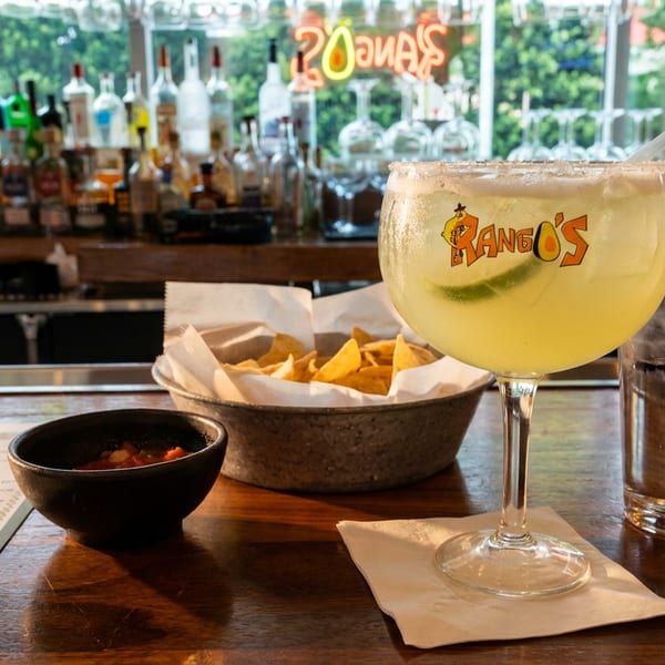 Margarita with lime and salt rim, chips, salsa, and water on a wooden bar.